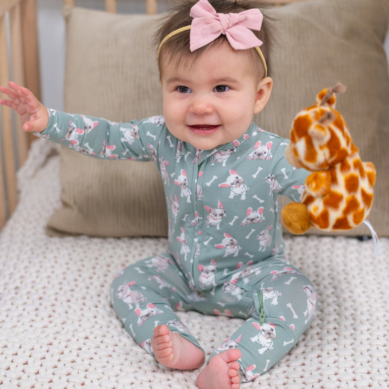 Baby in a patterned onesie with a giraffe toy on a bed