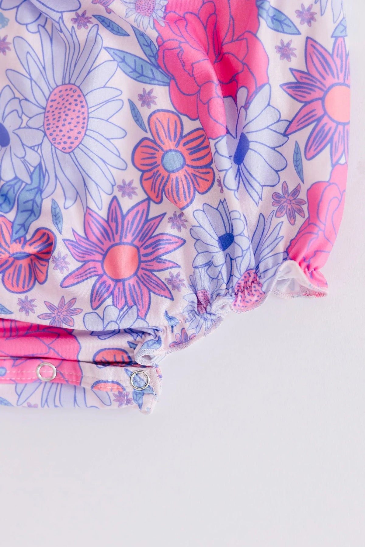 Close-up of pink and purple floral print ruffle cross back romper for baby with snap closures
