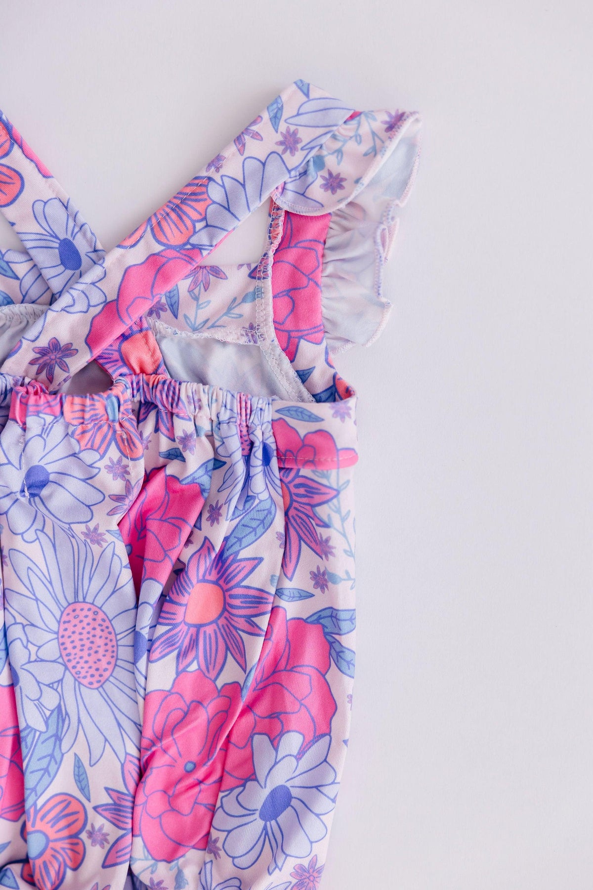 Close-up of pink and purple floral toddler ruffle cross back romper by Mila & Rose on white background