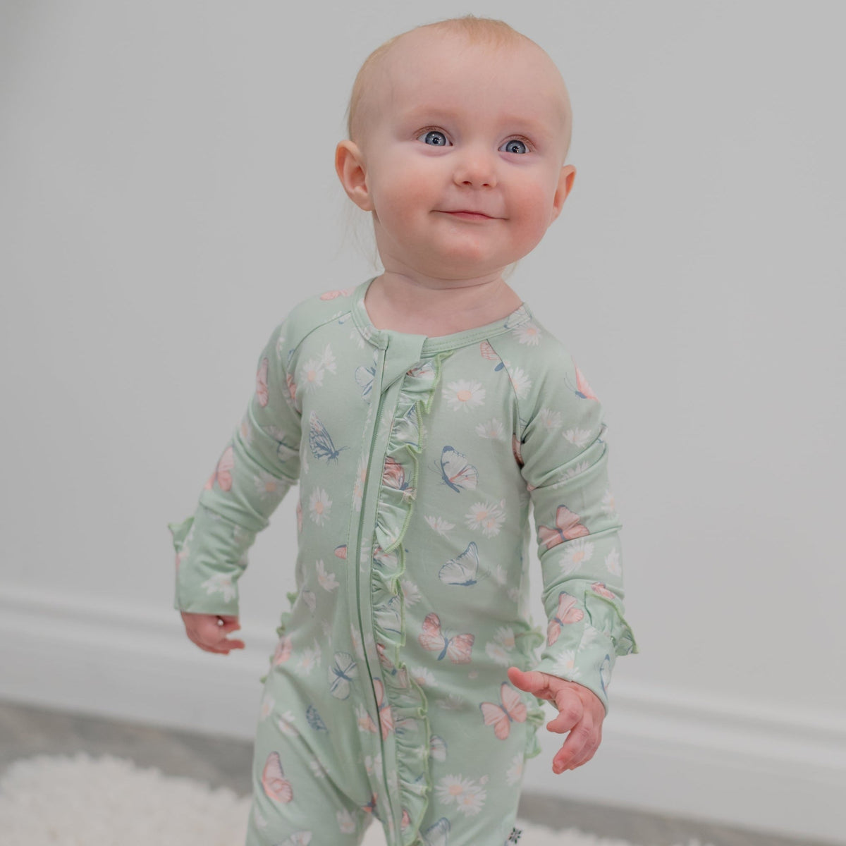 Baby wearing Mint Butterfly Daisy Bamboo Ruffle Baby Footie with butterfly and daisy print.