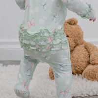 Mint Butterfly Daisy Bamboo Baby Footie with ruffles; baby in mint-green butterfly print outfit beside a teddy bear.