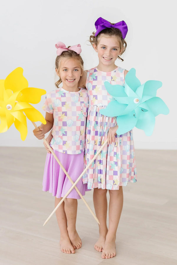 Girls pastel check ruffle pocket tee and dress set with purple bow and pink bow holding colorful pinwheels