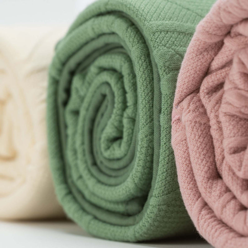 Three rolled Sage Knit Blankets by Goosewaddle® in various colors, emphasizing their softness and stylish look for newborns.