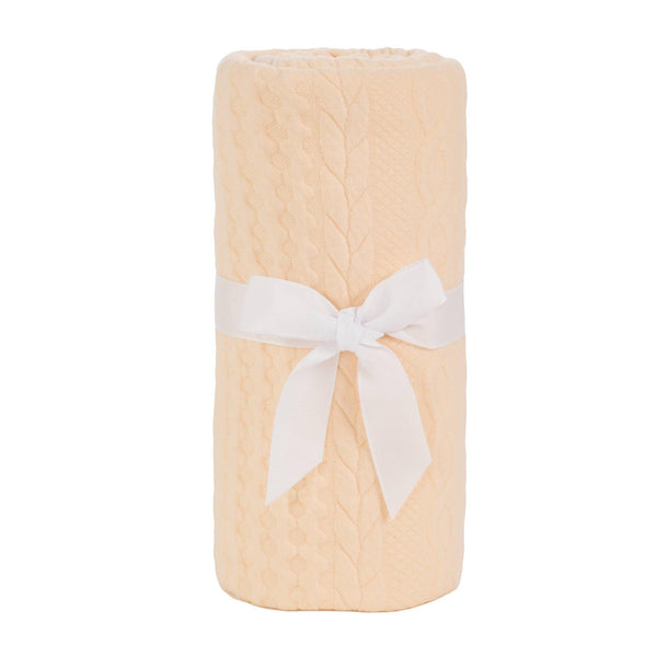 Soft baby knit blanket in light peach with cable knit pattern tied with a white ribbon for newborns