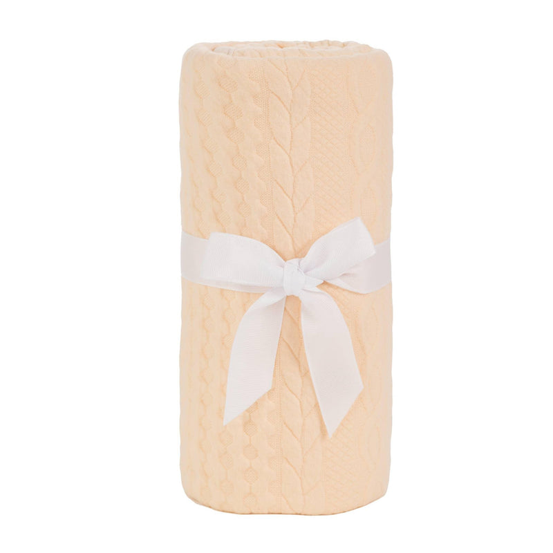 Soft baby knit blanket in light peach with cable knit pattern tied with a white ribbon for newborns