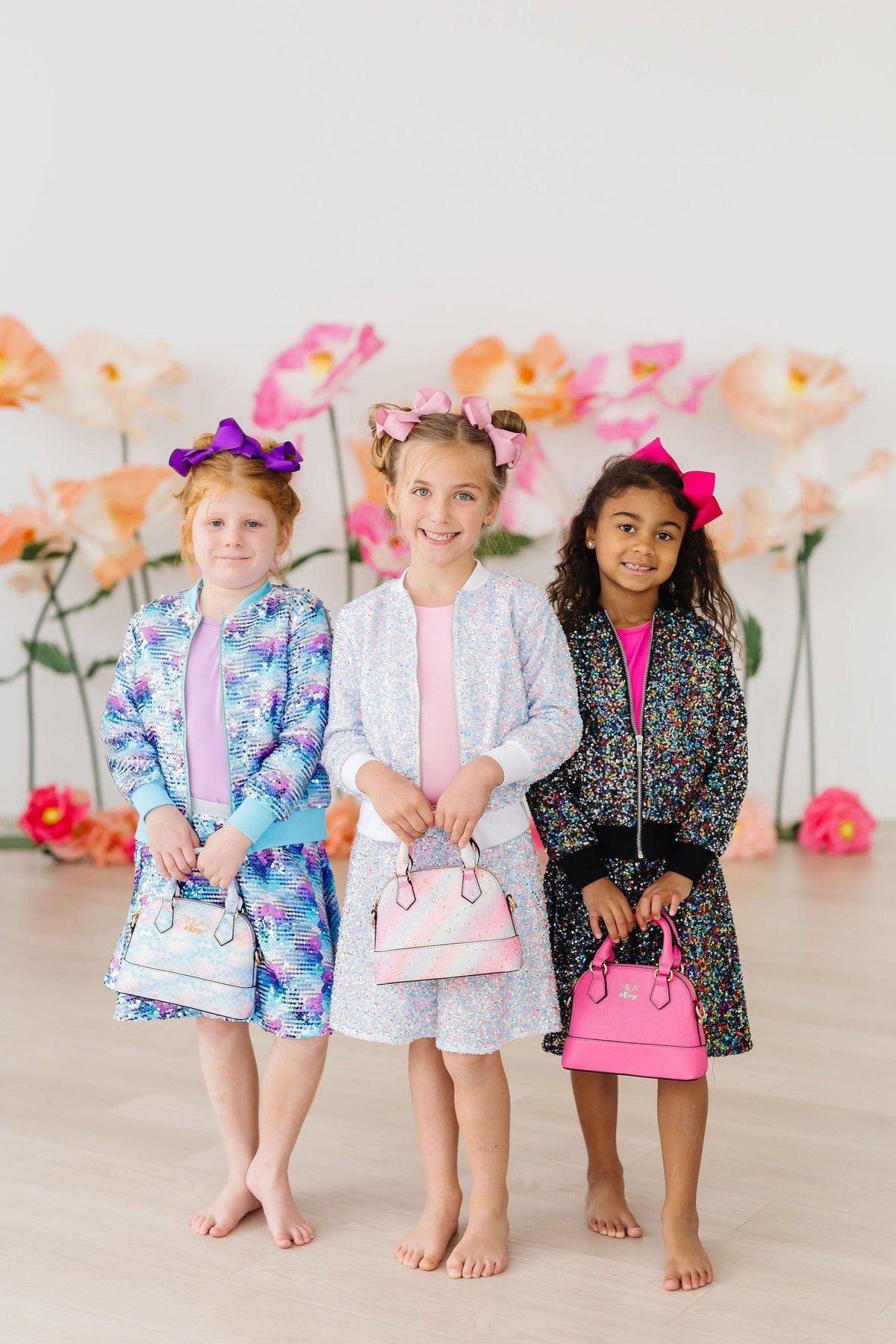 Three girls wearing colorful sequin jackets with matching skirts and holding handbags, long sleeve sequin jacket