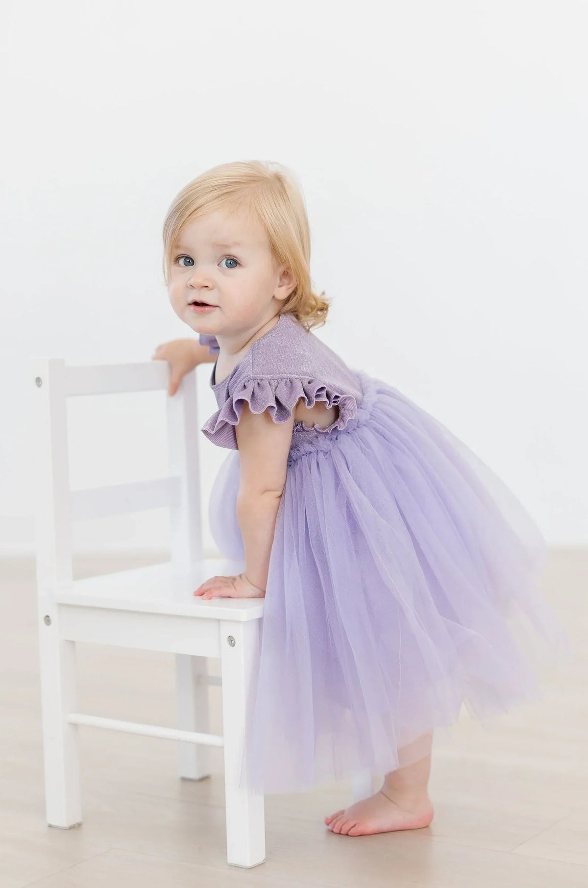 Toddler girl wearing lavender shimmer party dress for girls with ruffle sleeves and tutu skirt