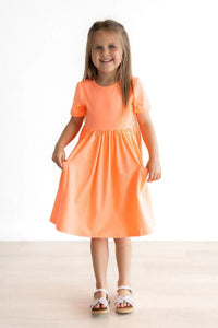 Young girl wearing orange short sleeve girls dress twirling and smiling