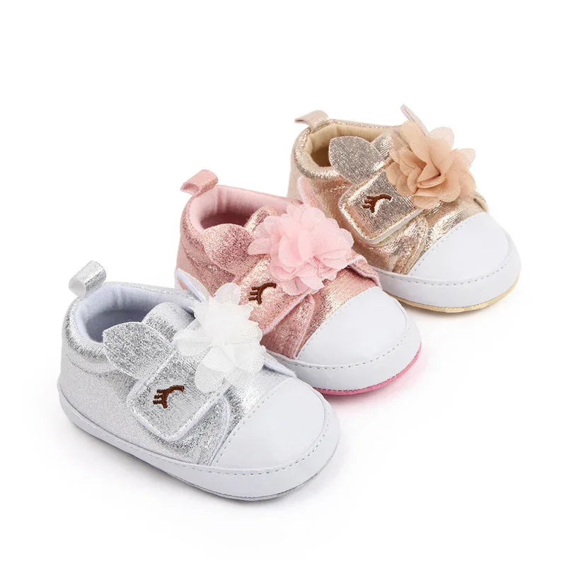 three pairs of glittery silver, pink, and gold soft sole baby shoes with flower and bear ear details for infants