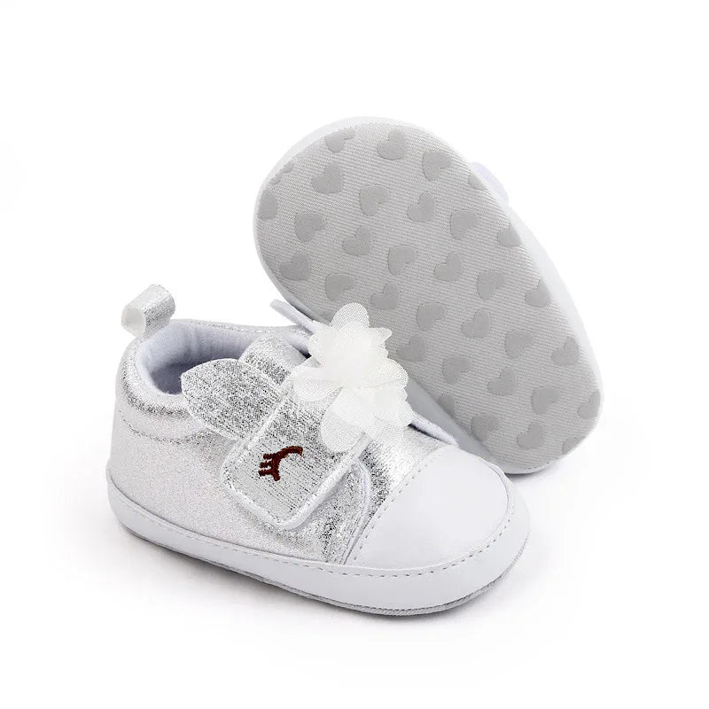 Silver soft sole baby shoes with white flower detail for infants, one shoe standing and one showing sole
