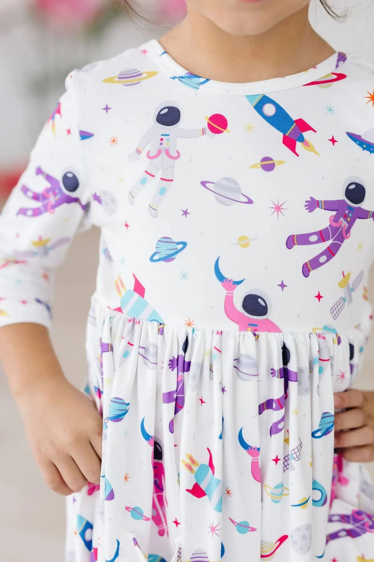 young girl wearing white space print twirl dress for girls with astronauts and rockets holding skirt