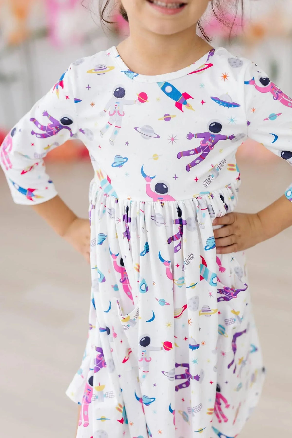 Girl wearing white space print twirl dress for girls with colorful astronaut and rocket designs posing with hands on hips