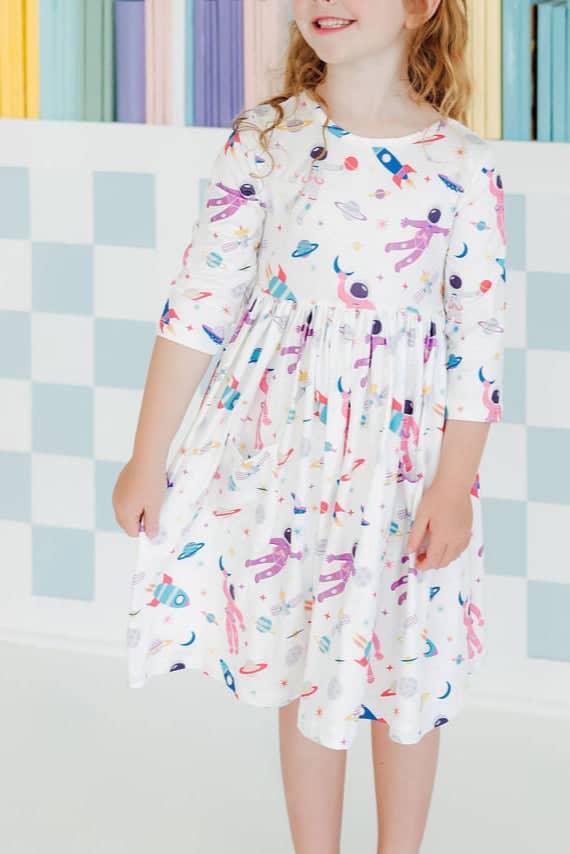 Girl wearing white space print twirl dress for girls with 3/4 sleeves smiling indoors