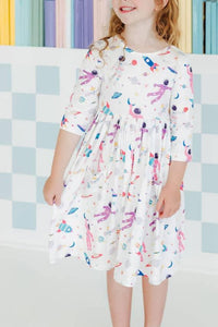 Girl wearing white space print twirl dress for girls with 3/4 sleeves smiling indoors