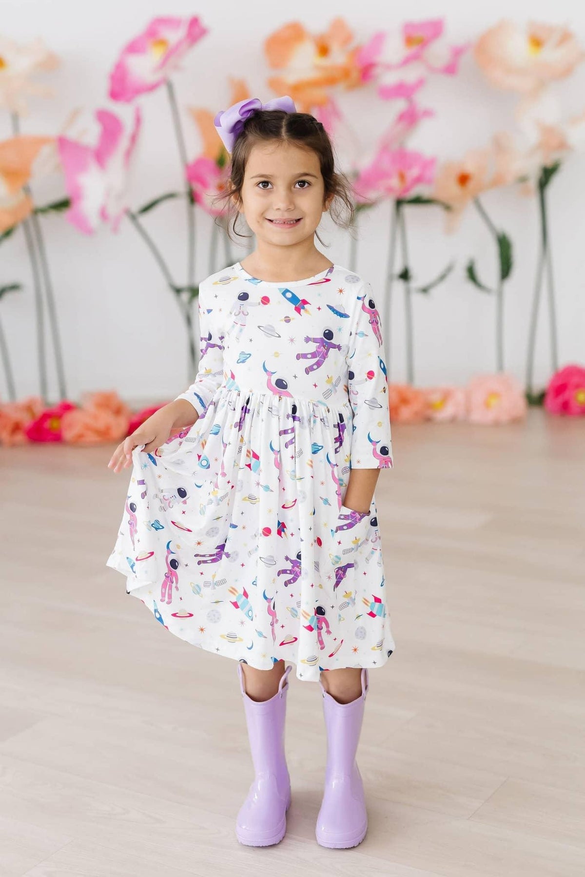 young girl wearing white space print twirl dress for girls holding skirt and smiling indoors