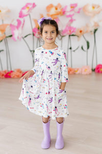 young girl wearing white space print twirl dress for girls holding skirt and smiling indoors