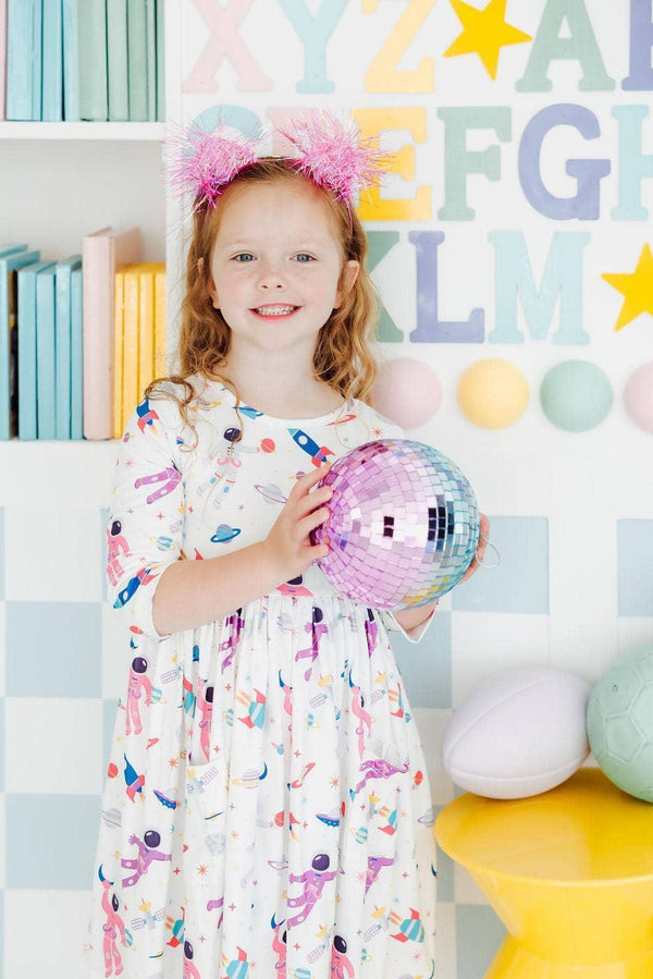 smiling girl wearing white space print twirl dress for girls holding a pink disco ball indoors