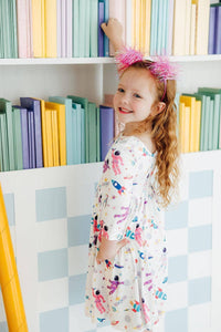young girl wearing white space print twirl dress for girls reaching for books on shelf