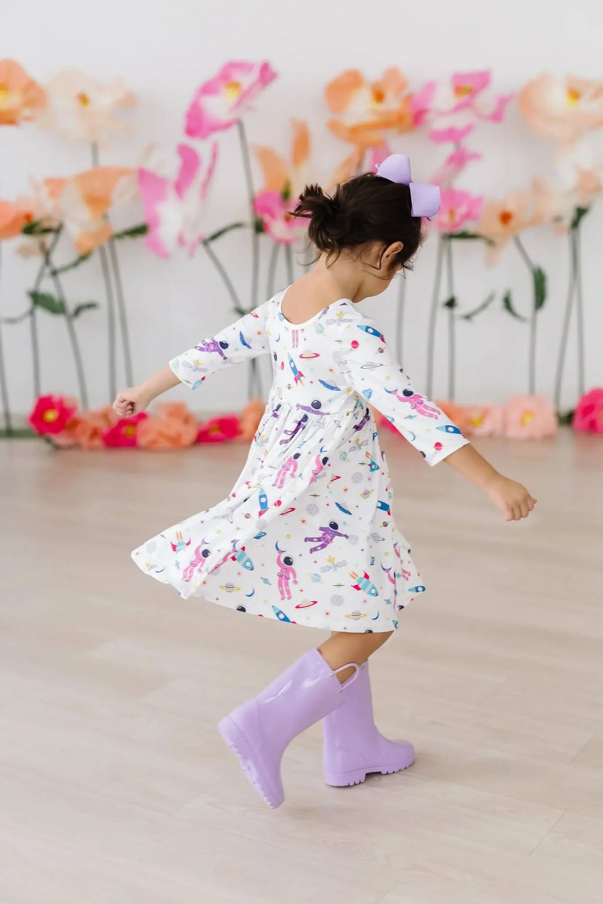 Young girl wearing white space print twirl dress for girls and purple boots spinning indoors