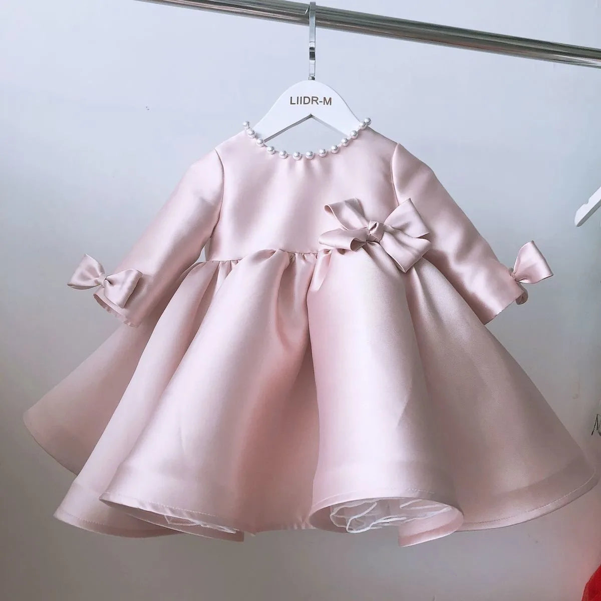 Baby pink special occasion dress with pearl neckline and bow details on sleeves and waist for infants