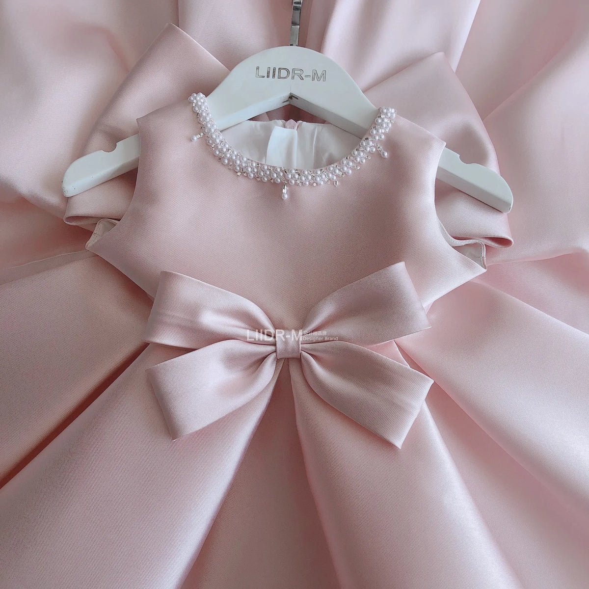 baby pink special occasion dress with pearl neckline and large bow detail for infants