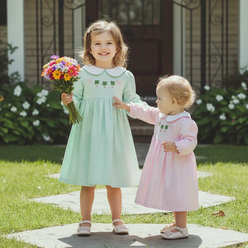Two girls wearing St. Patrick's Day dress for little girls in green and pink holding a bouquet outdoors