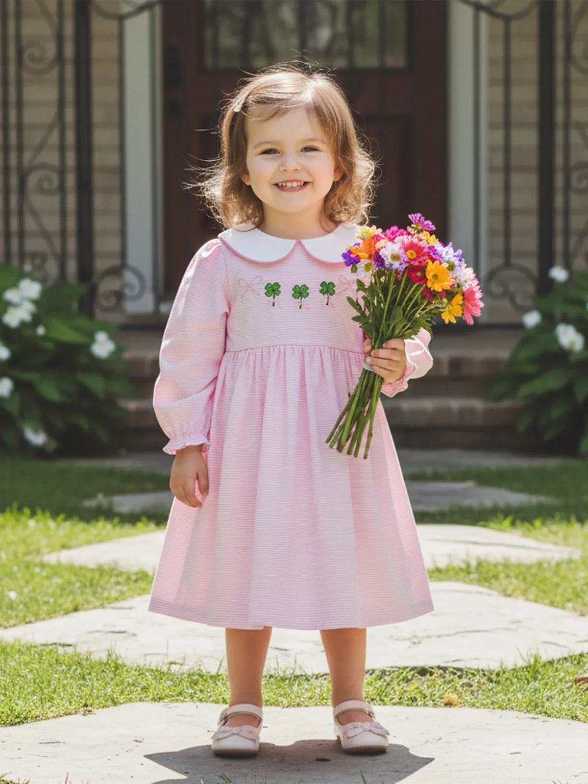 Toddler girl wearing pink St. Patrick's Day dress for little girls holding a colorful flower bouquet outdoors