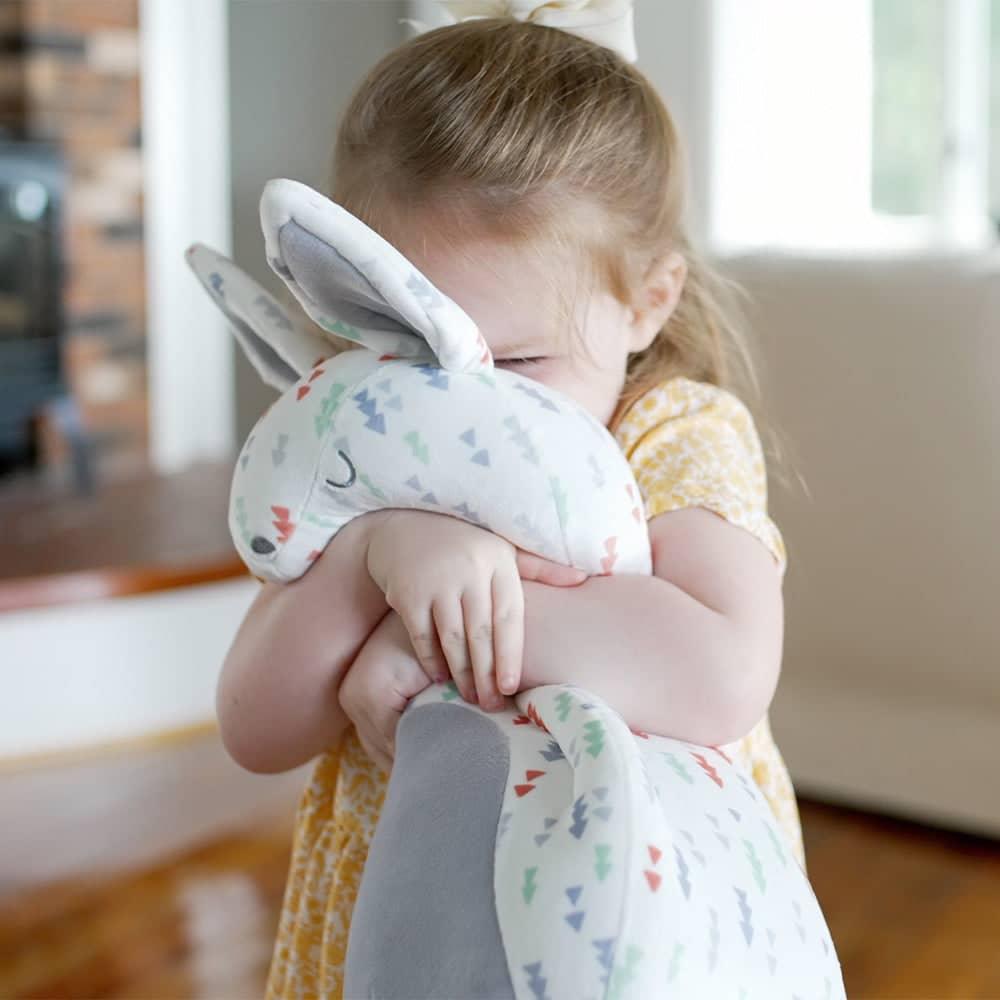 White patterned plush comfort toy with pastel triangles hugged by toddler girl, super soft baby comfort toy