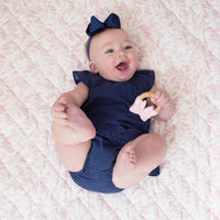 smiling baby girl wearing navy blue outfit and headband lying on pink super soft baby play mat holding teether