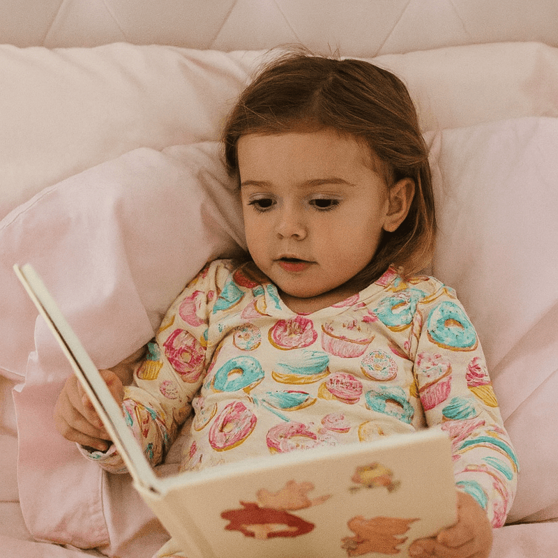 Child in pajamas reading a book on a pink bed