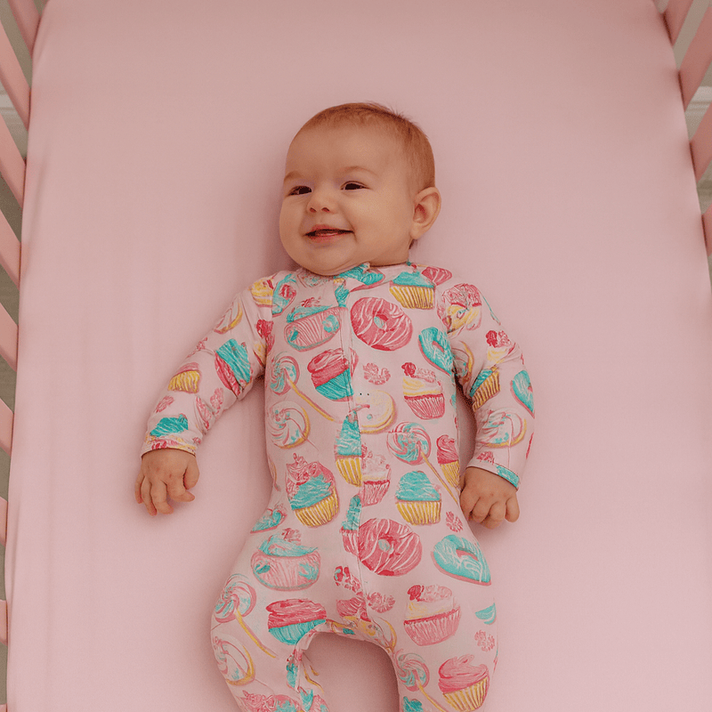 Baby wearing a colorful onesie with dessert patterns on a pink surface