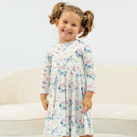 Smiling girl in knee-length Watercolor Butterfly Swirly Girl Dress with empire waist and long sleeves, butterfly print.