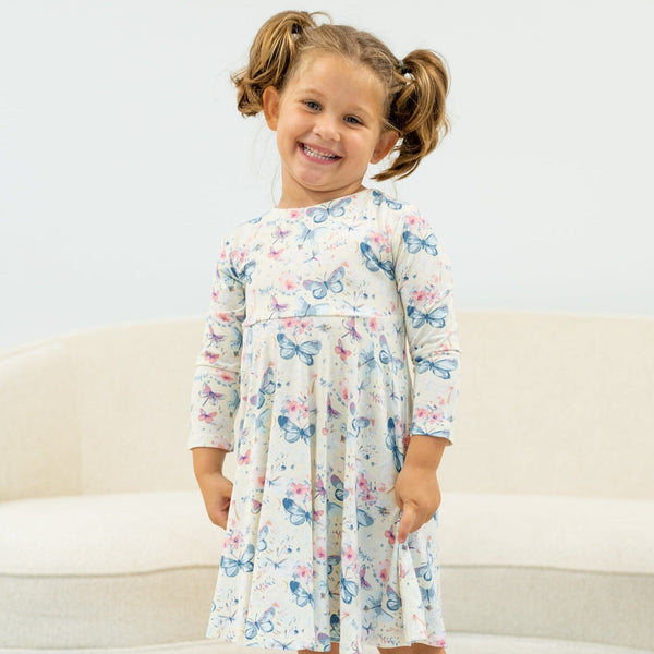 Smiling girl in knee-length Watercolor Butterfly Swirly Girl Dress with empire waist and long sleeves, butterfly print.