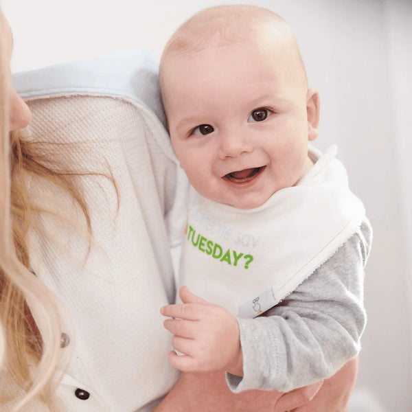 smiling baby wearing white and green taco baby bib set held by adult in gray and white clothing