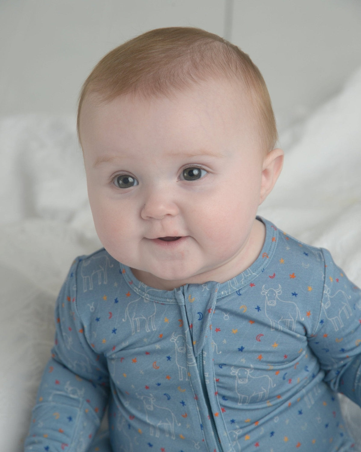 Baby wearing soft blue Taurus zodiac bamboo footie with bull and star pattern and front zipper.