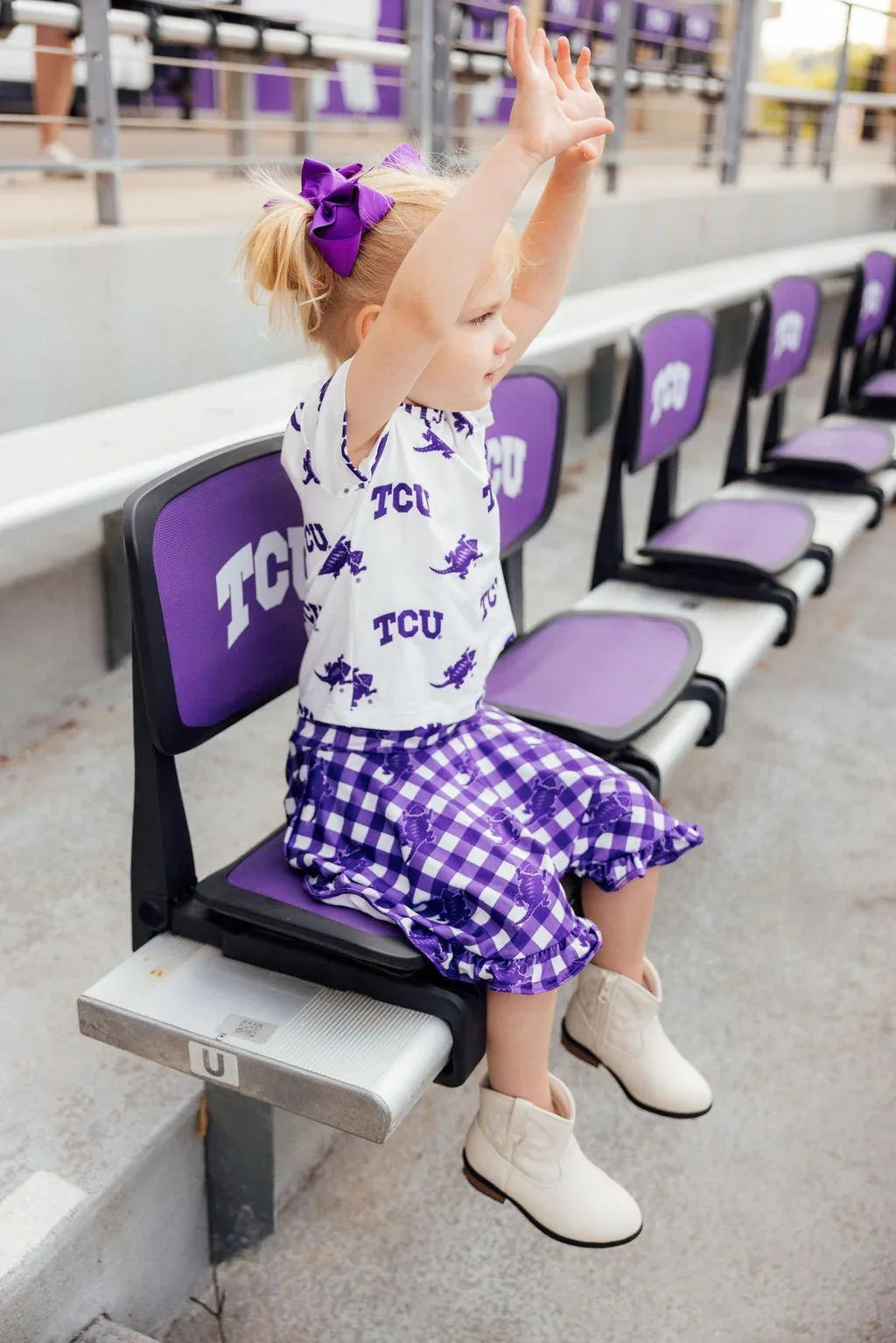 Toddler girl wearing purple and white TCU girl ruffle skort with matching TCU top and bow