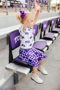 Toddler girl wearing purple and white TCU girl ruffle skort with matching TCU top and bow