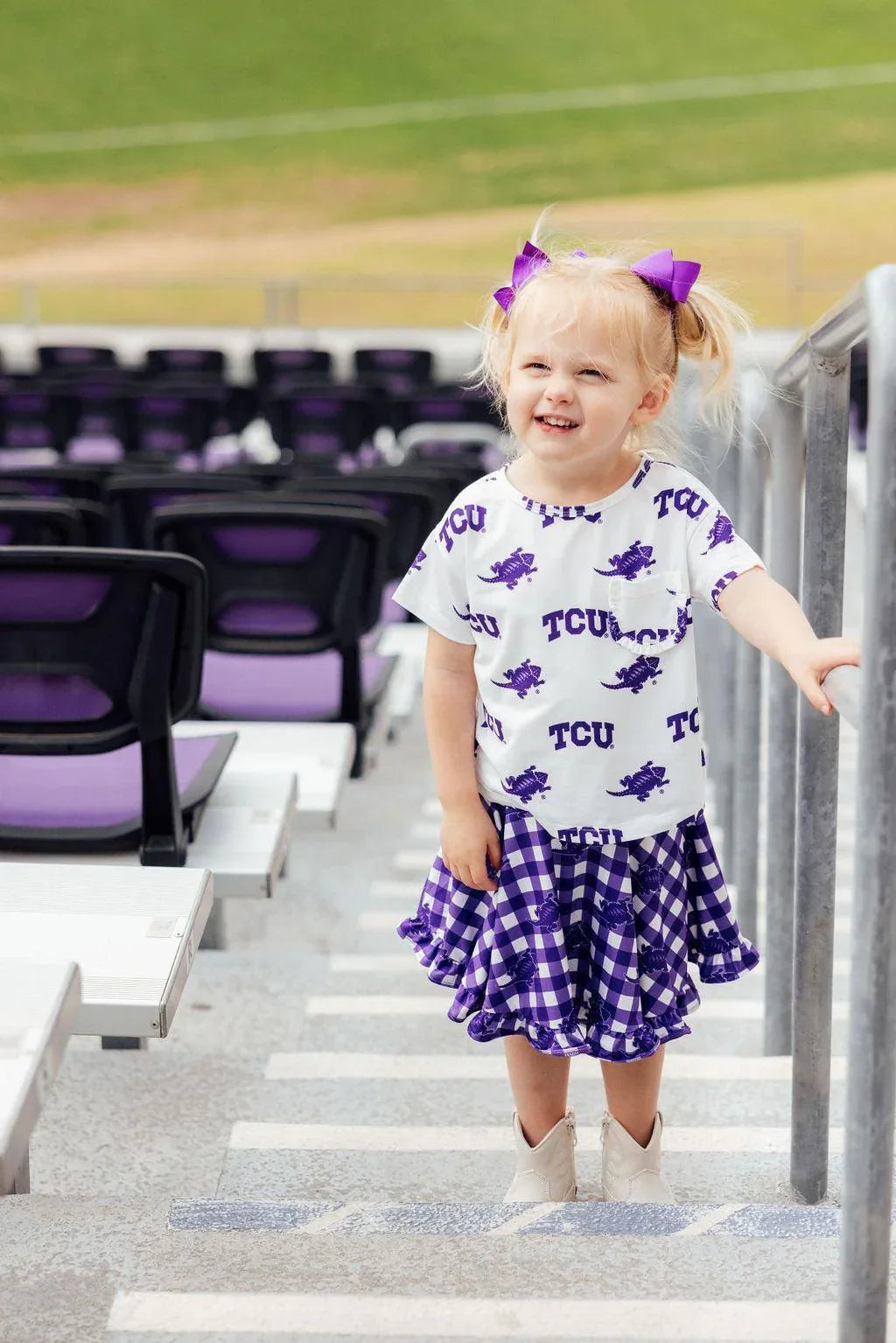 Toddler girl wearing purple and white TCU girl ruffle skort with matching TCU shirt and purple hair bows
