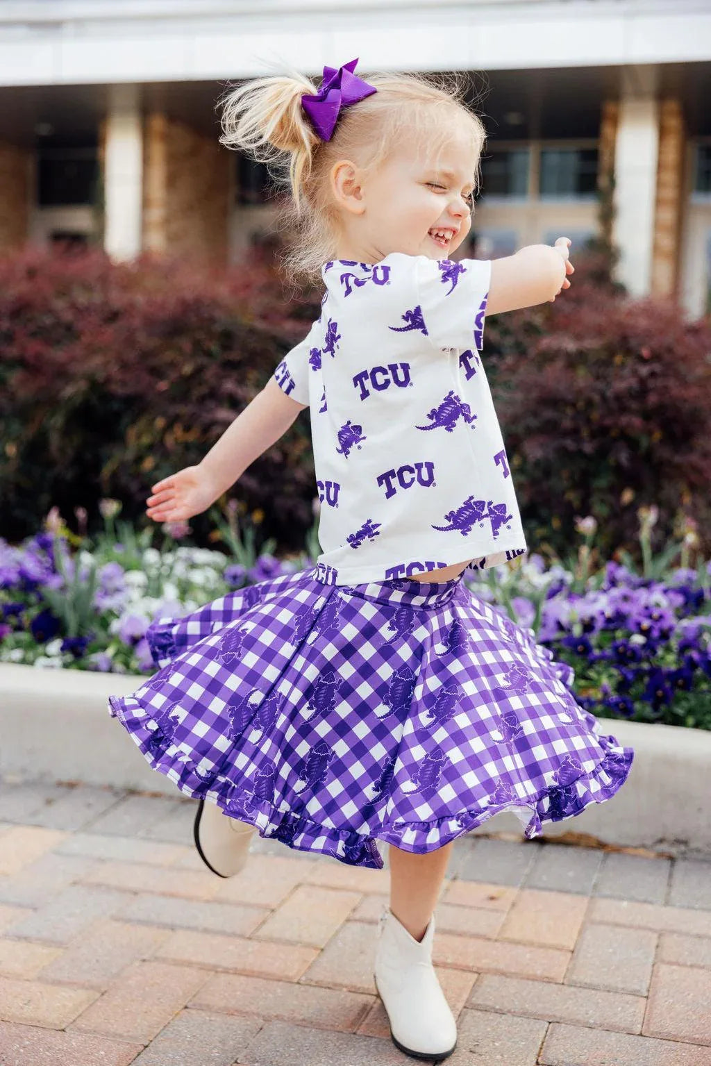 Toddler girl wearing purple and white TCU girl ruffle skort with matching TCU shirt and purple bow