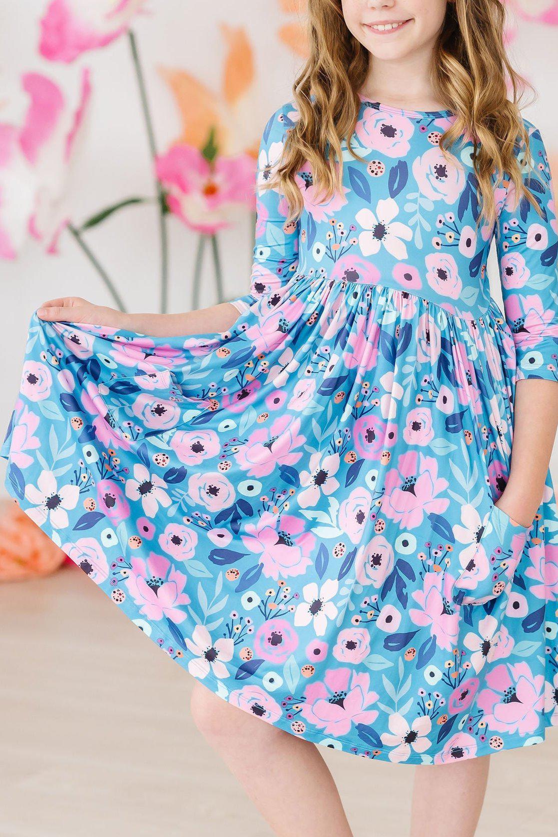 Girl wearing teal floral twirl dress for girls holding out skirt and smiling indoors
