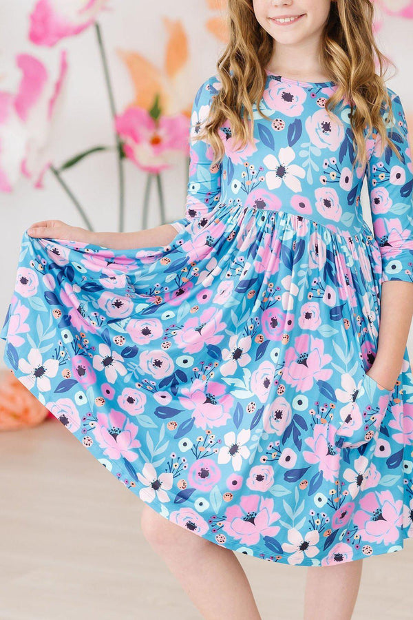 Girl wearing teal floral twirl dress for girls holding out skirt and smiling indoors