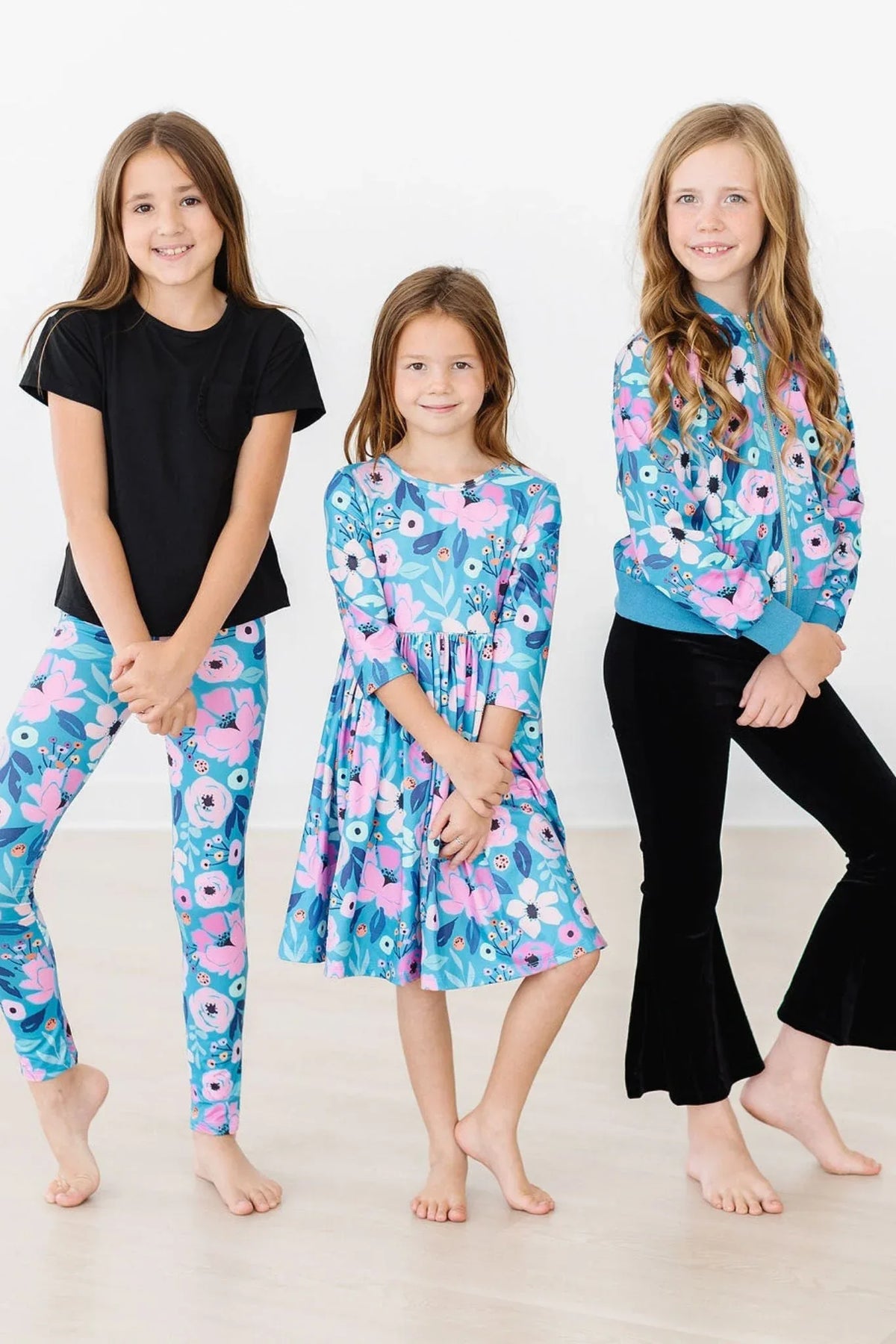 Girl wearing teal floral twirl dress for girls standing barefoot with two other girls in matching floral leggings and jacket