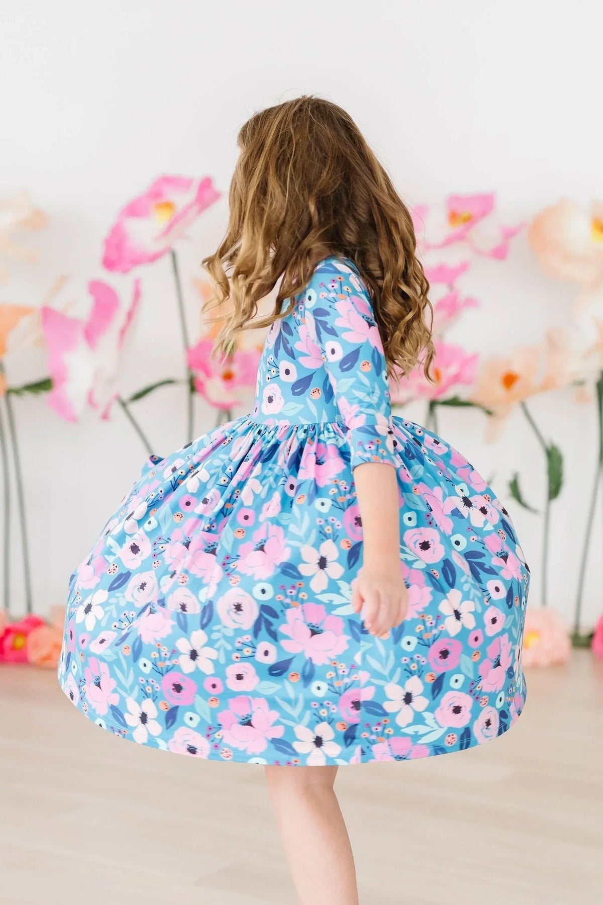 Young girl wearing teal floral twirl dress for girls spinning in a bright room with flowers