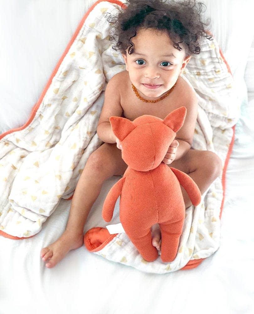 Infant holding terracotta fox baby gift set plush toy sitting on white baby blanket with orange trim