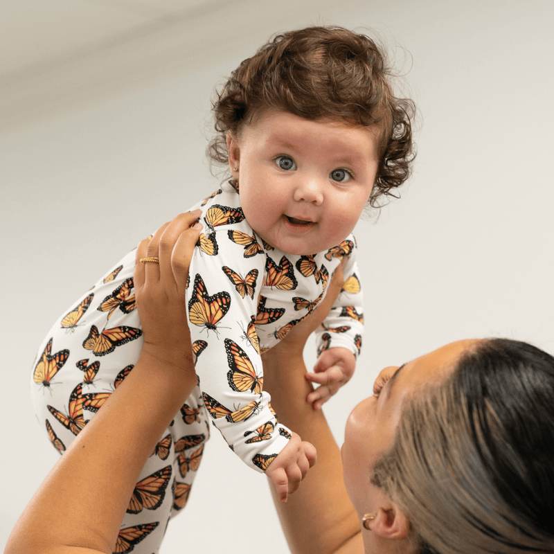 Baby wearing a butterfly-patterned outfit with a woman holding it against a white background