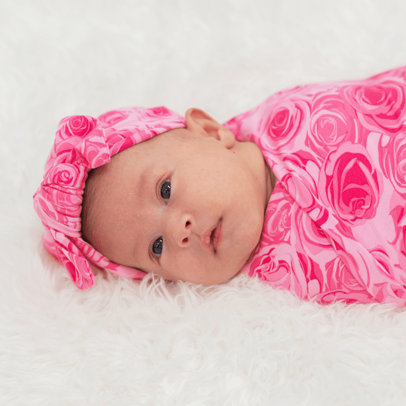 Newborn in This Must Be Love Swaddle, pink Palm Beach-inspired rose pattern with matching headband.