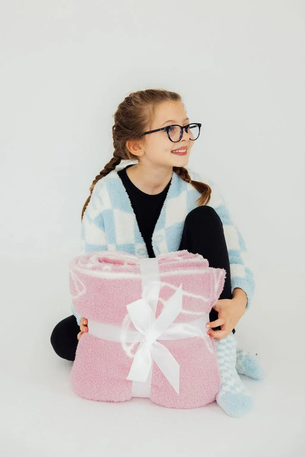 young girl holding pink throw blanket with white ribbon in cozy setting
