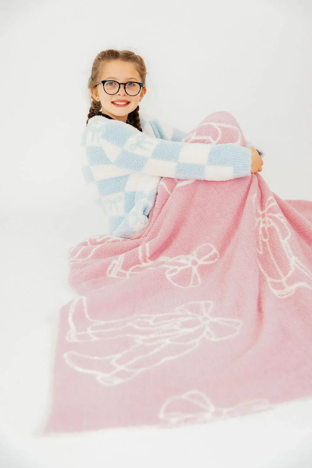 Girls pink throw blanket with white bow designs wrapped around young girl in blue checkered sweater