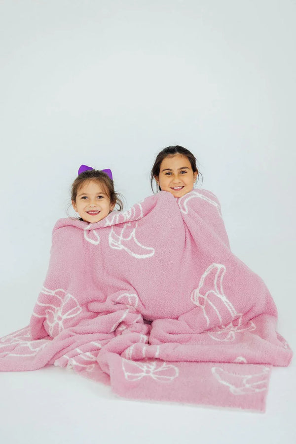 Two young girls wrapped in a pink Mila & Rose throw blanket with white outline bows