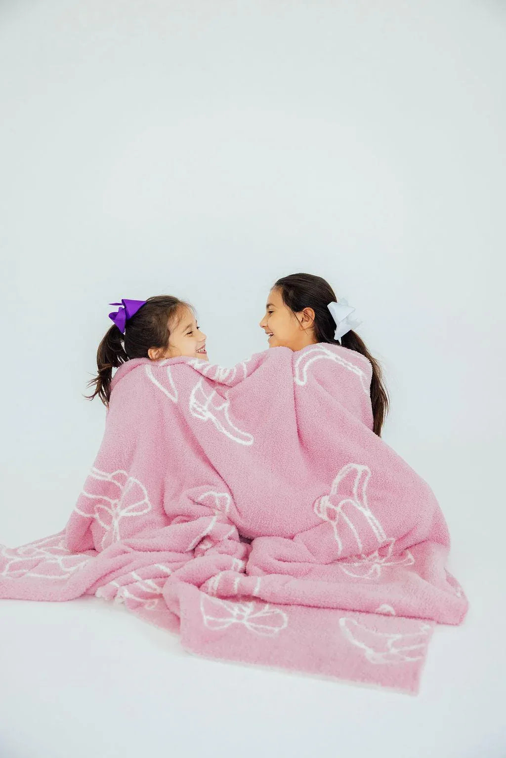 Girls pink throw blanket with white bow patterns wrapped around two kids cozy and soft